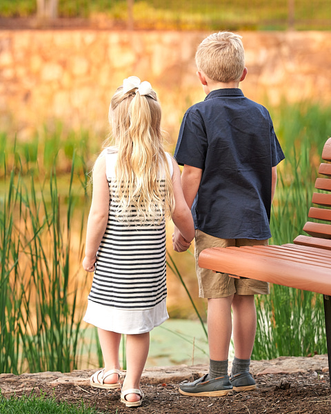Siblings holding hands and looking at the pond